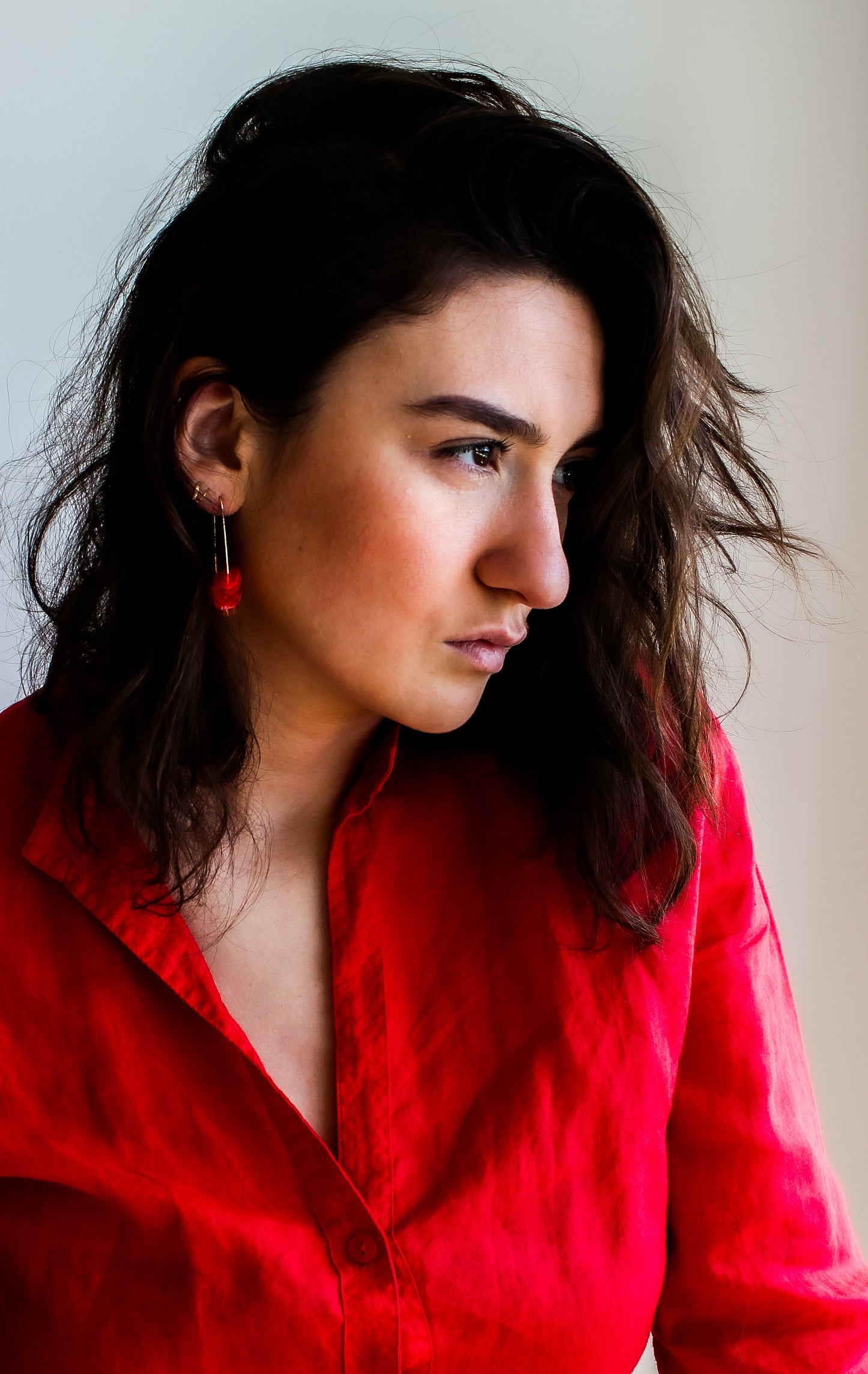 A woman in a red shirt wears sustainable 14k gold filled earrings with coral petals, handmade from recycled materials.