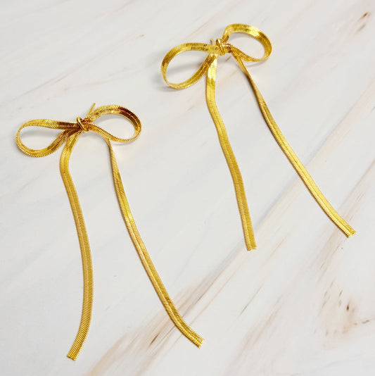 Two elegant gold bows on a white background, showcasing long drop earrings with a modern design and sophisticated charm.