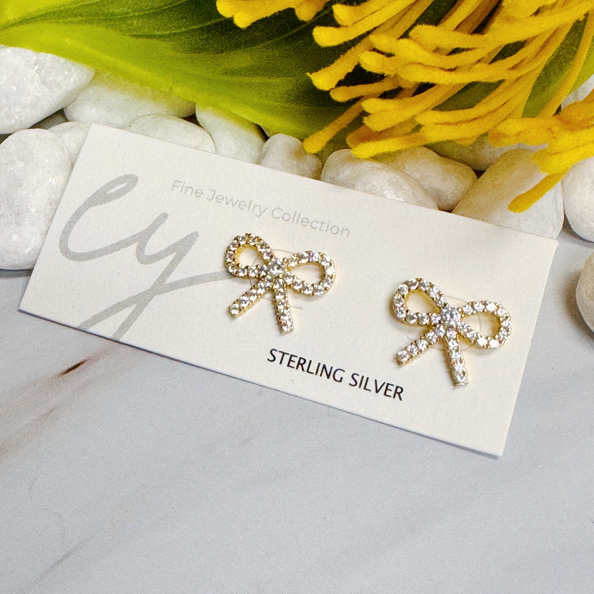 Gold bow earrings displayed on a card, made of 18k gold plated sterling silver, adding classic charm to any outfit.