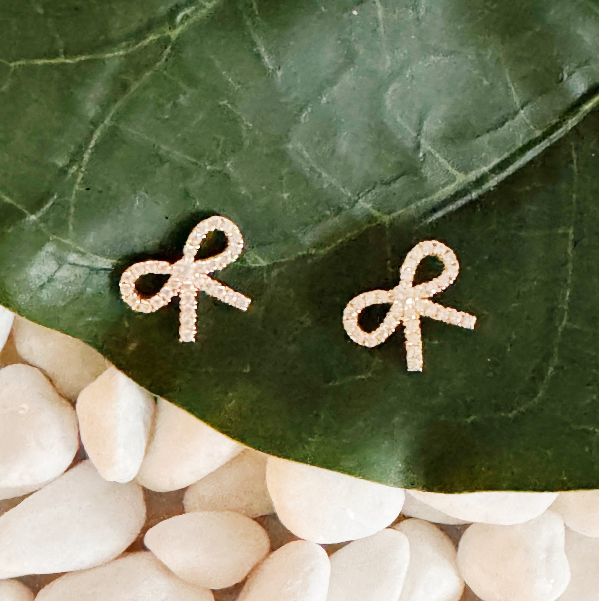 A pair of gold bow stud earrings on a leaf, showcasing their elegant design and shine, crafted from sterling silver