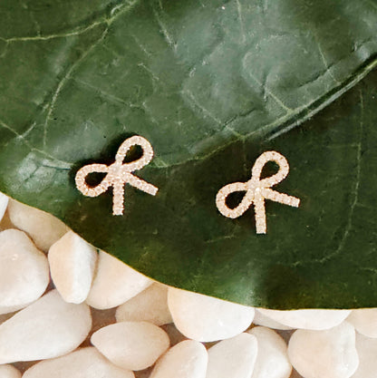 A pair of gold bow stud earrings on a leaf, showcasing their elegant design and shine, crafted from sterling silver