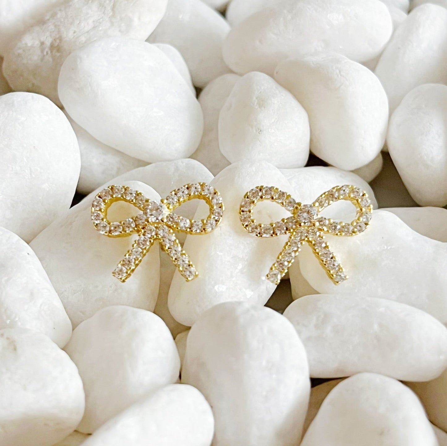  Two gold bow stud earrings on white stones, crafted from 18k gold plated sterling silver with cubic zirconia accent