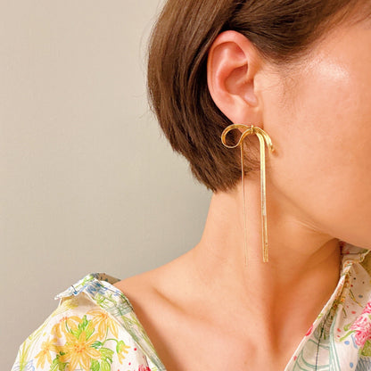 Close-up of a woman’s ears adorned with stylish long drop bow earrings, showcasing their modern gold design.