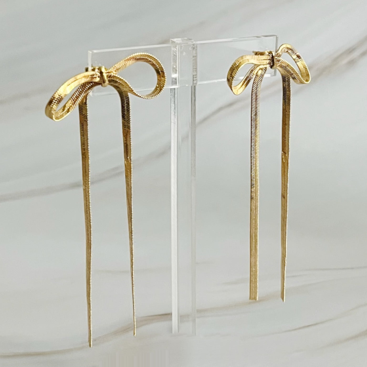 Two gold bows against a white background, highlighting chic long drop earrings with a unique shape and modern appeal.