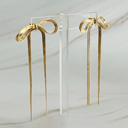 Two gold bows against a white background, highlighting chic long drop earrings with a unique shape and modern appeal.