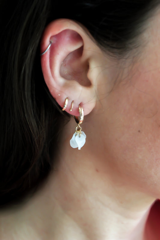A woman wearing sustainable 14k gold filled huggers with a white flower pendant, handmade from recycled materials.