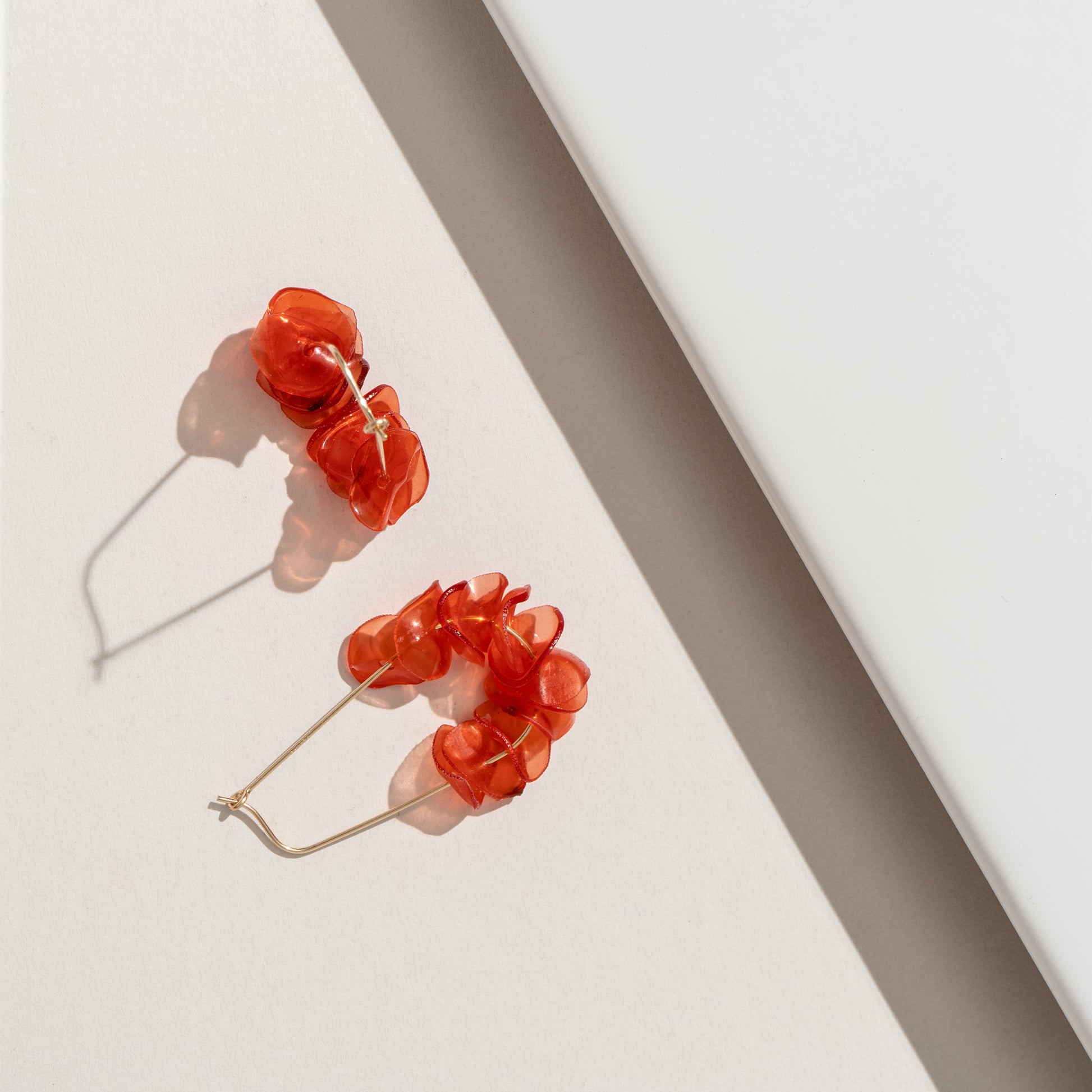 Orange coral petal earrings on a white surface, made from recycled metals, lightweight, and handmade in Arlington, VA