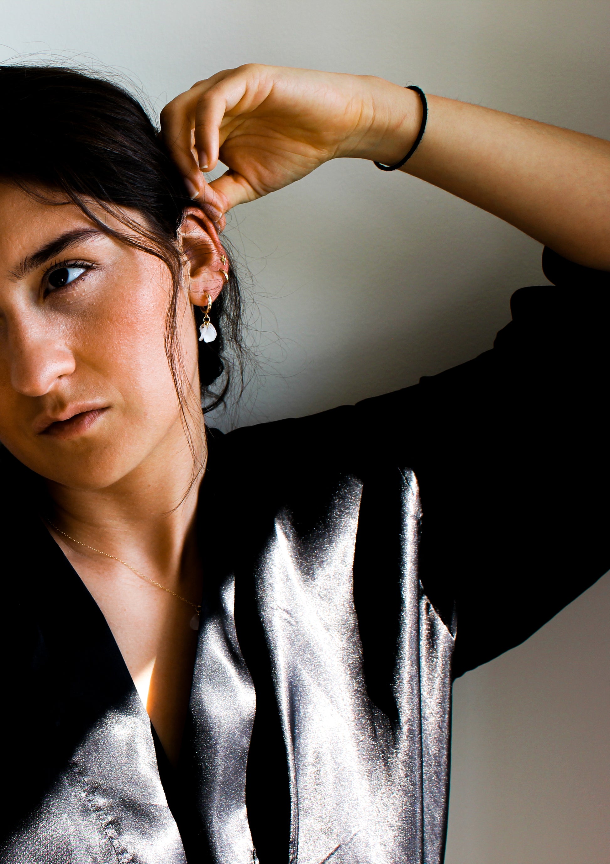A woman in a black shirt and tie, wearing sustainable gold-filled huggers with a white flower pendant.