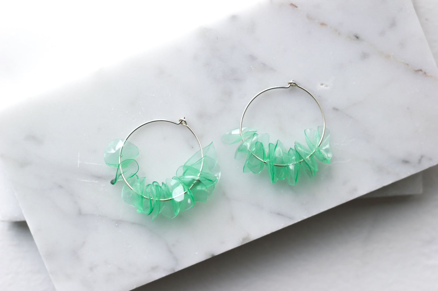 Green glass earrings with aquamarine petals on sterling silver hoops, displayed on a marble surface. Handmade and lightweight.
