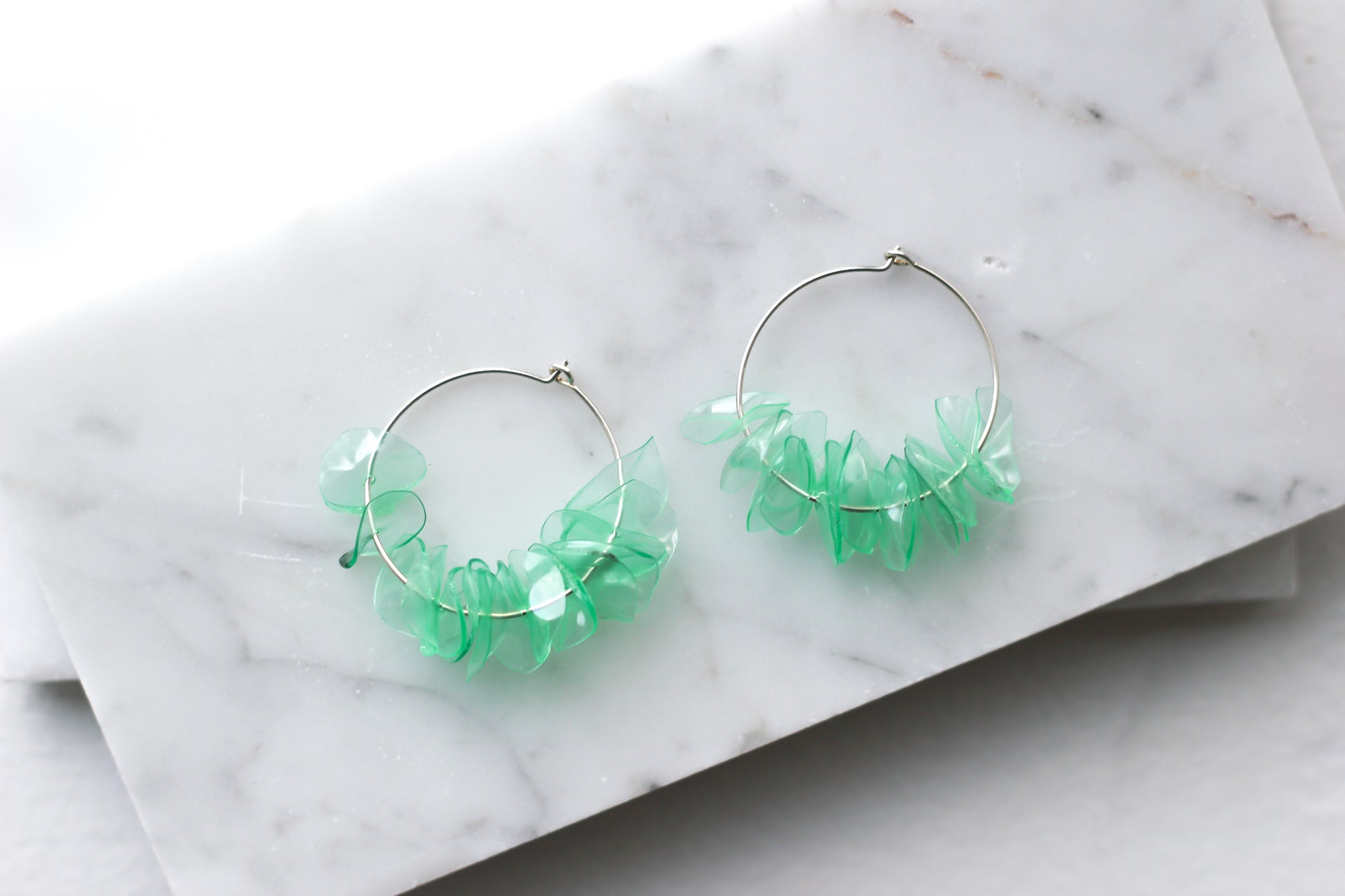 Green glass earrings with aquamarine petals on sterling silver hoops, displayed on a marble surface. Handmade and lightweight.
