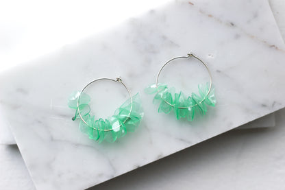 Green glass earrings with aquamarine petals on sterling silver hoops, displayed on a marble surface. Handmade and lightweight.
