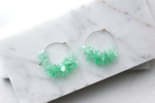 Green glass earrings with aquamarine petals on sterling silver hoops, displayed on a marble surface. Handmade and lightweight.
