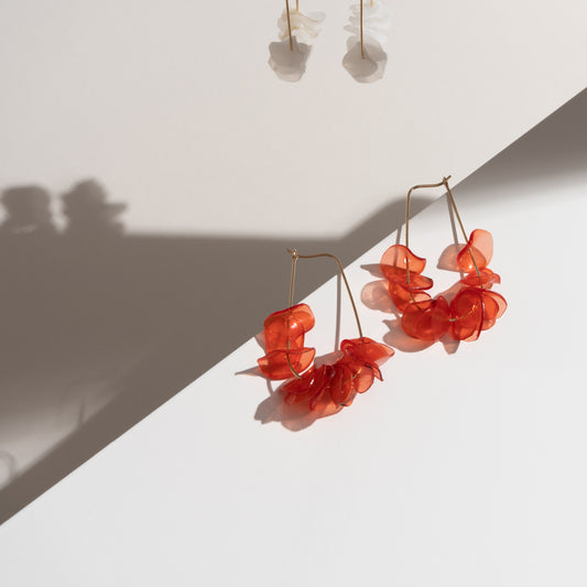 A pair of lightweight orange earrings with coral petals on a white surface, handmade from recycled materials in Arlington, VA.