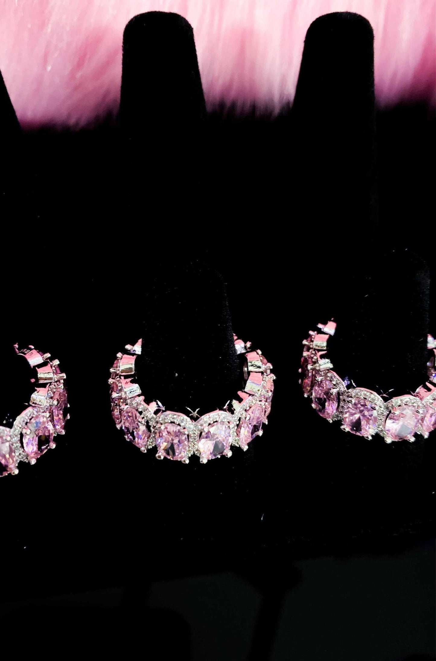 Three pairs of pink diamond earrings displayed on a sleek black
surface, showcasing elegance and luxury.
