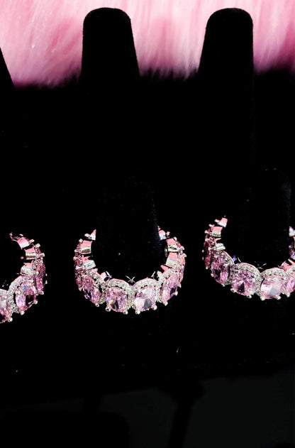 Three pairs of pink diamond earrings displayed on a sleek black
surface, showcasing elegance and luxury.
