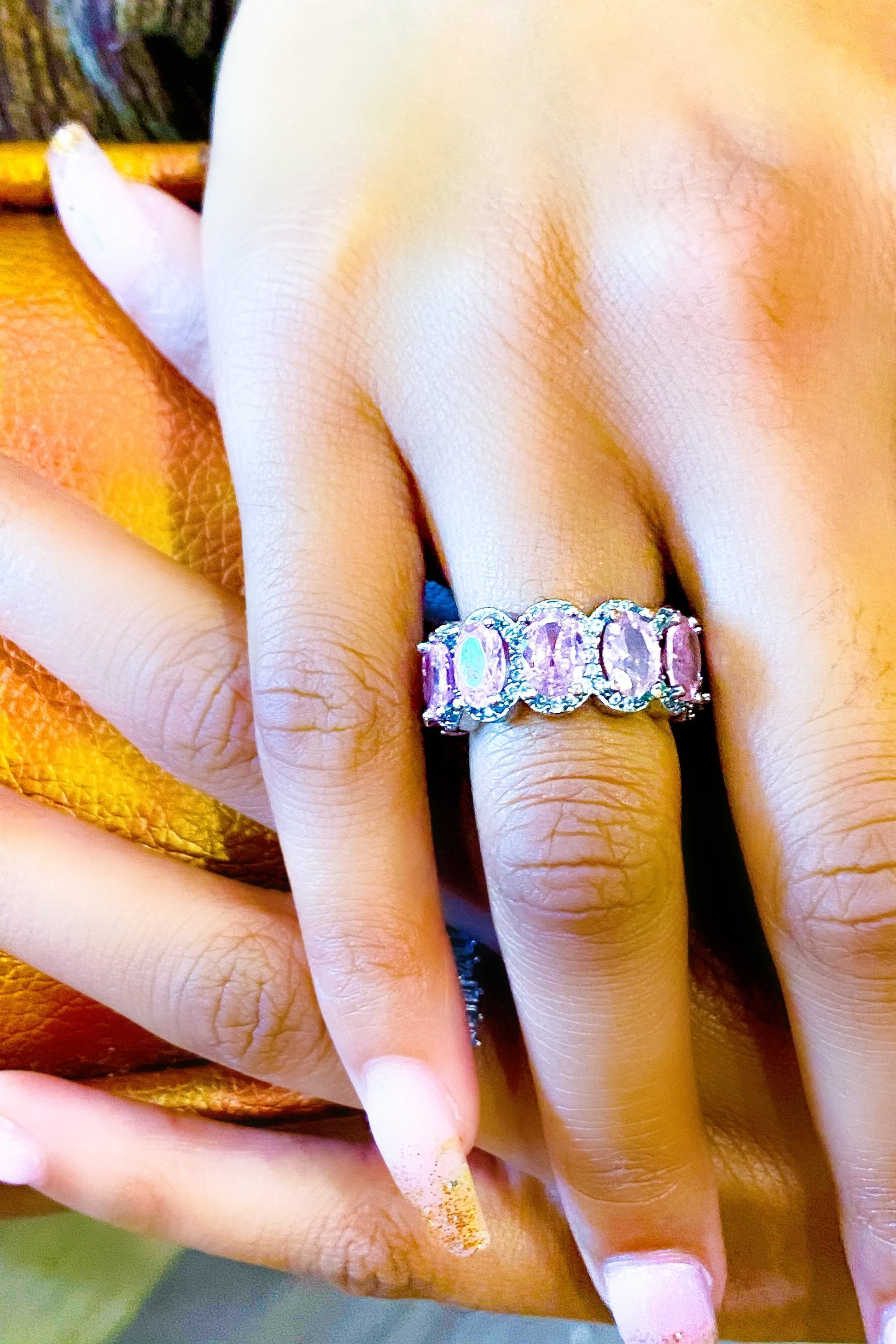 A close-up of a woman's hand holding a pink and purple
eternity ring made of high polished 14K white gold.
