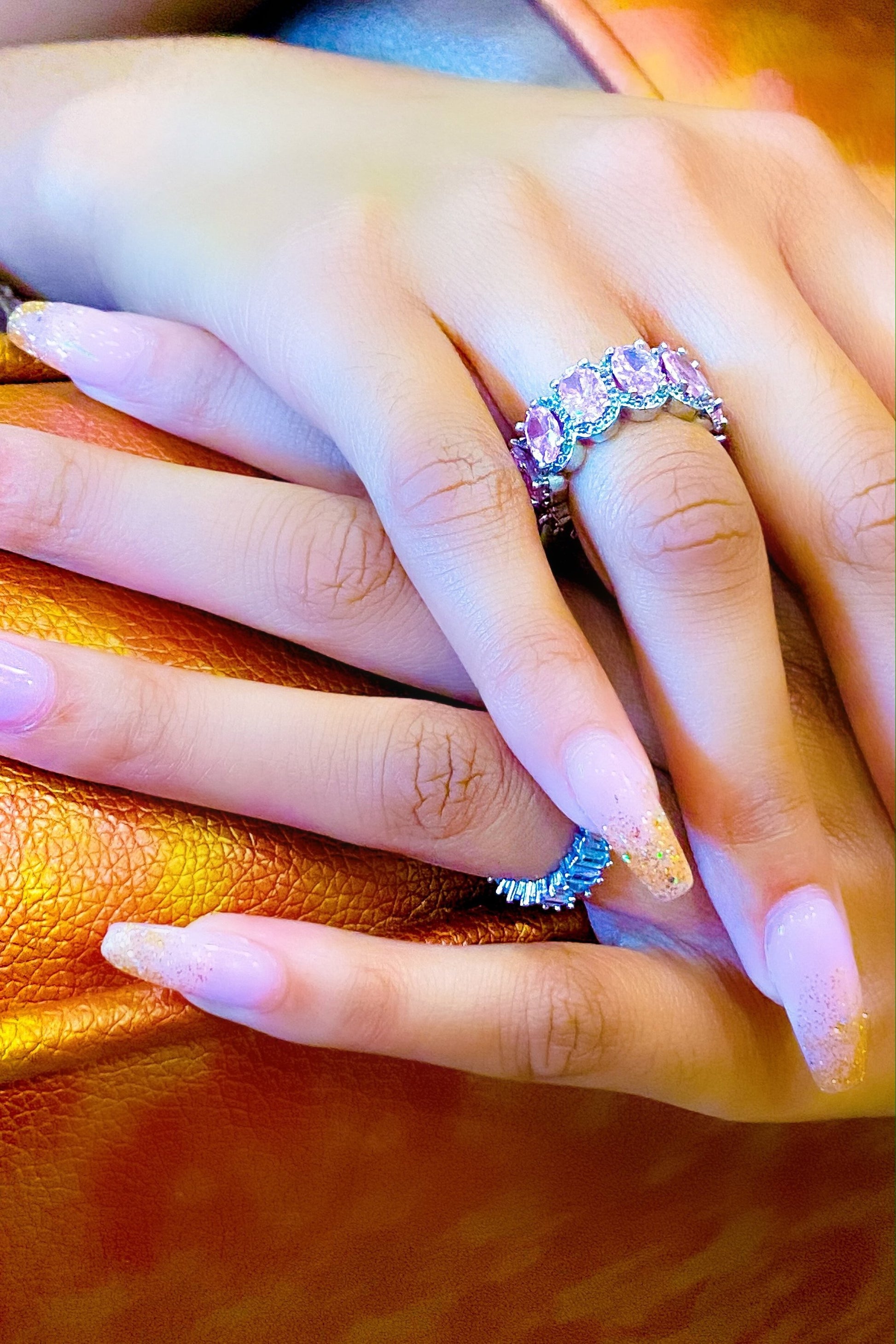 A close-up of a woman's hand holding a pink and purple
eternity ring made of high polished 14K white gold.
