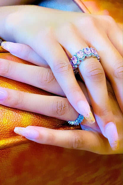 A close-up of a woman's hand holding a pink and purple
eternity ring made of high polished 14K white gold.
